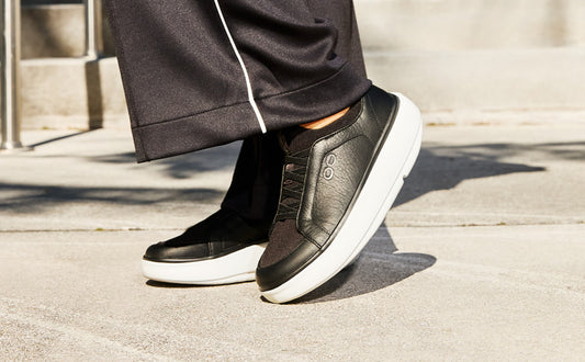 Black sneakers with white soles worn by a person on a concrete surface | lifestyle