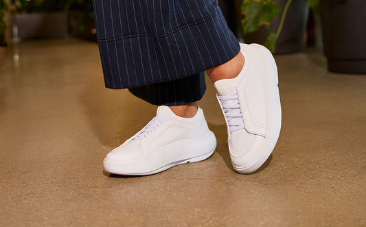 White sneakers worn with dark pinstripe pants on a brown floor | lifestyle