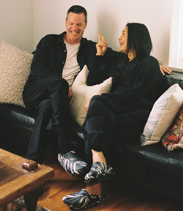 Nok Suntaranon and Greg on a couch, laughing. They are both wearing the TILIT x OOFOS limited-edition Off Hours clogs.