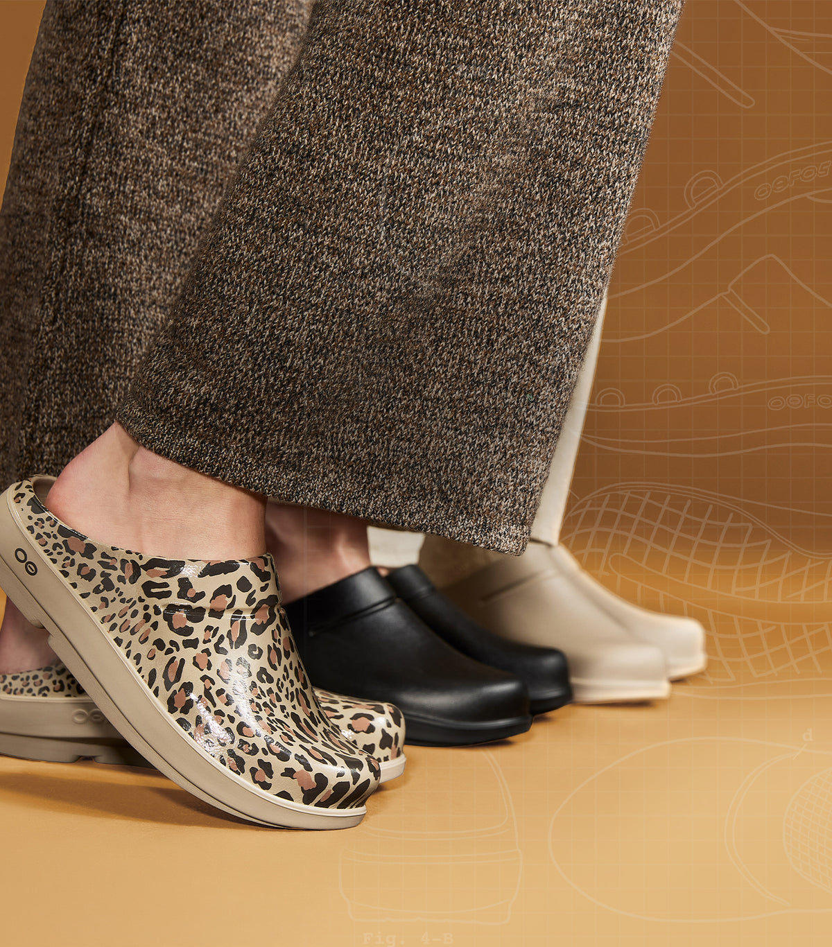 Leopard print clog shoe in the foreground, with black and off-white clogs lined up behind it on a warm tan studio background. A person's lower legs and feet are visible wearing the shoes.