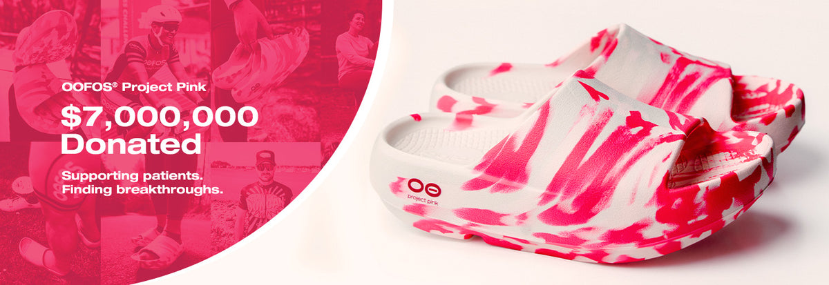 A pair of white slip-on clogs with a bright pink abstract paint-splatter pattern, shown on a white background with a pink graphic overlay on the left side containing text for 'OOFOS Project Pink'.
