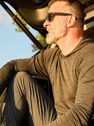 Man wearing sunglasses and a brown shirt sitting in a vehicle with a clear sky background