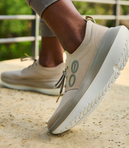 Beige casual shoes with white soles worn outdoors on a concrete surface.