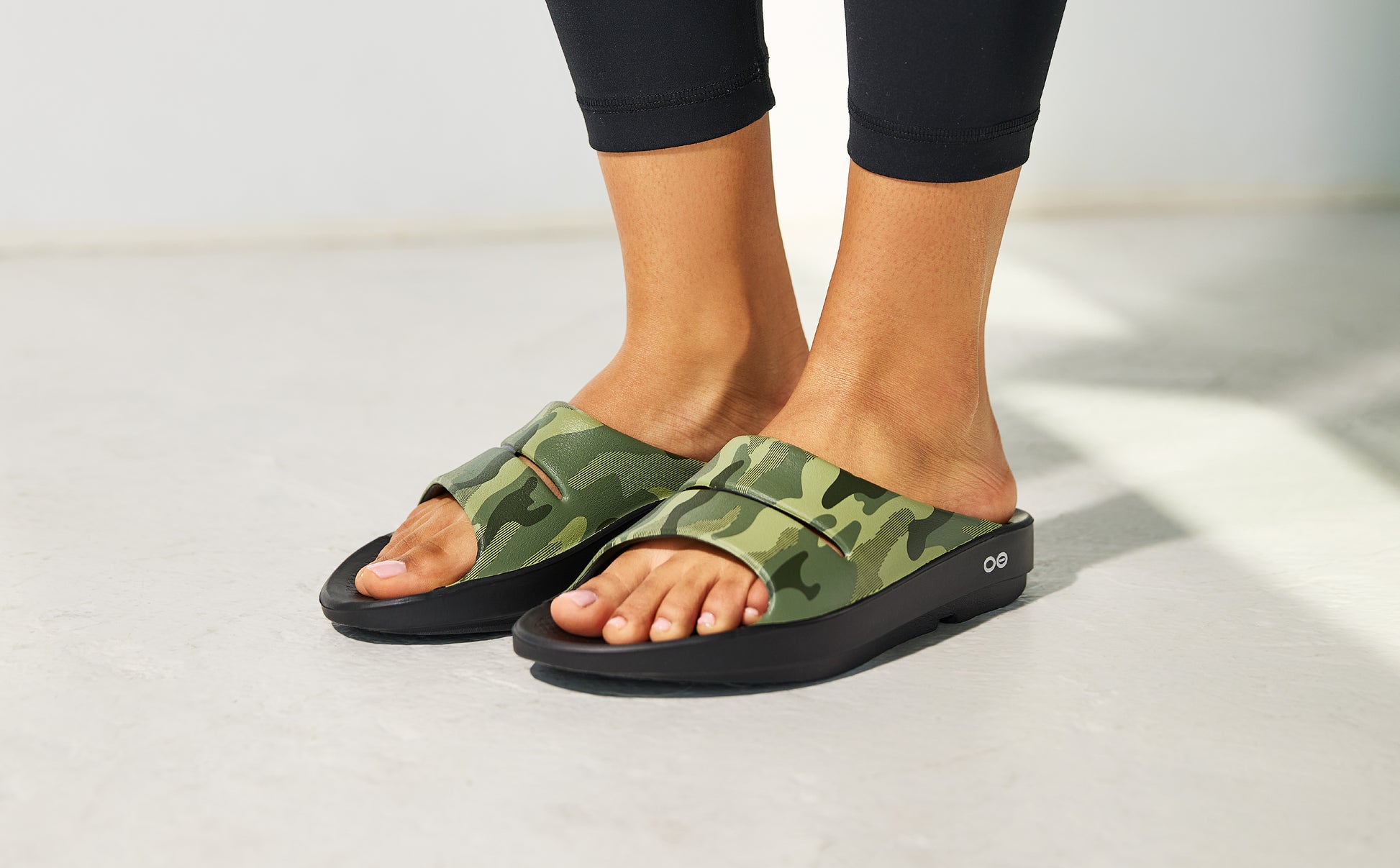 Green camouflage sandals worn with black leggings on a light background | lifestyle