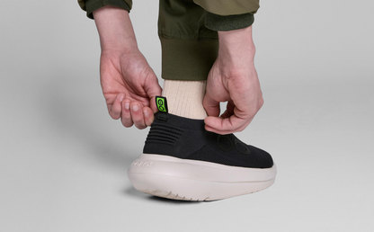 Men's OOmy Zen - Chalk Black model adjusting back of shoe in studio | lifestyle