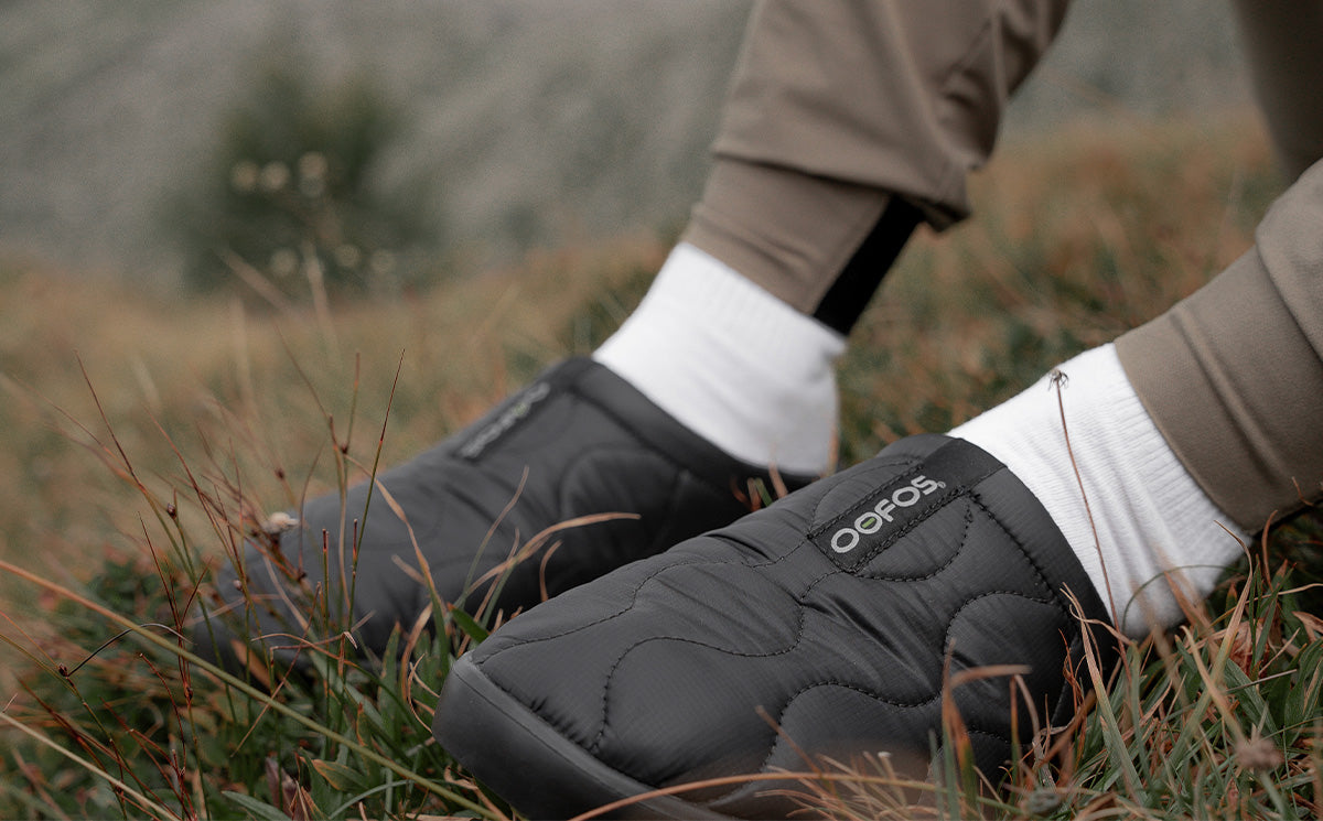Men's OOcoozie Thermo Mule - Black model sitting outside in grass wearing shoes | lifestyle
