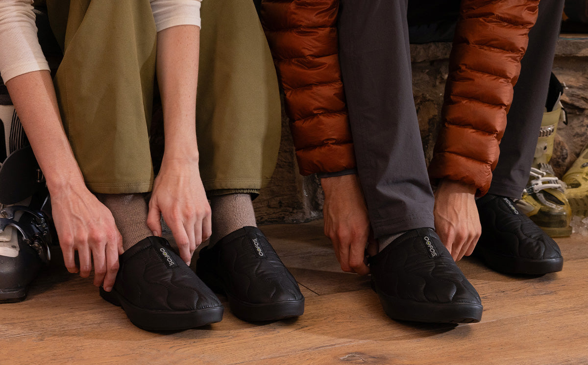 Men's OOcoozie Thermo Mule - Black models sitting inside putting shoes on | lifestyle