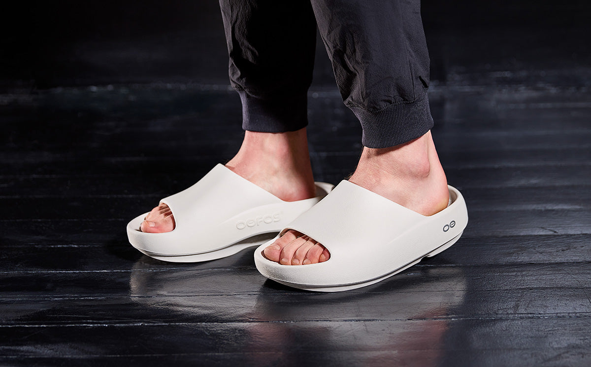 White sandals worn on a dark wooden floor | lifestyle