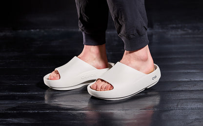 White sandals worn on a dark wooden floor | lifestyle