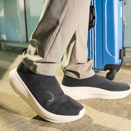Person wearing black shoes with a blue suitcase in the background