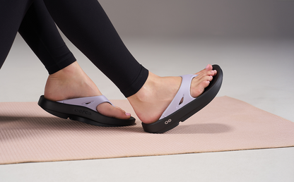 Person wearing black sandals with purple straps on a yoga mat | lifestyle