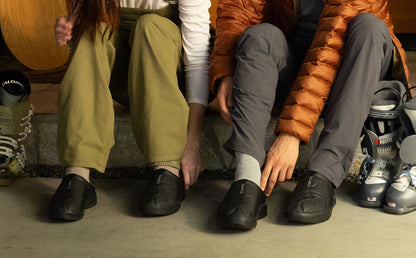 Women's OOcoozie Thermo Mule - Black models sitting inside adjusting shoes | lifestyle