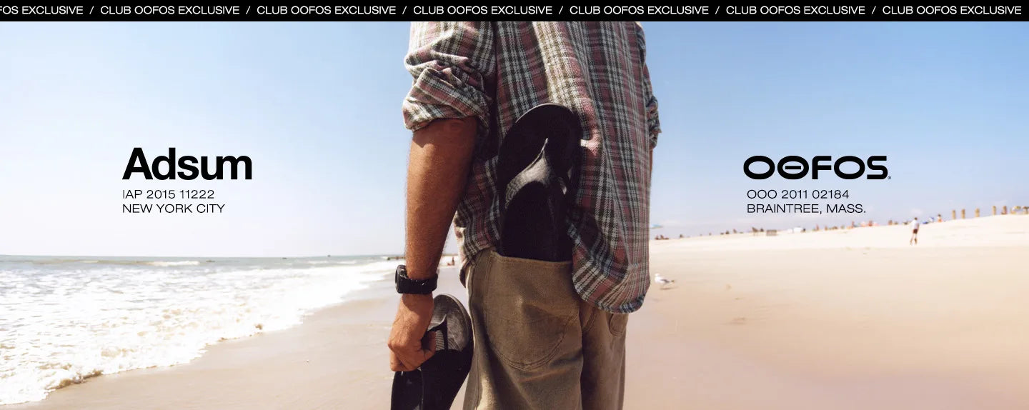 A man standing on a sandy beach holding OOFOS × Adsum OOriginal Limited Sandals, wearing a plaid shirt and khaki pants. The image features “Adsum: IAP 2015 11222 NEW YORK CITY” branding on the left and “OOFOS: OOO 2011 02184 Braintree, Mass” branding on the right, with a black banner at the top reading “CLUB OOFOS EXCLUSIVE” repeated.