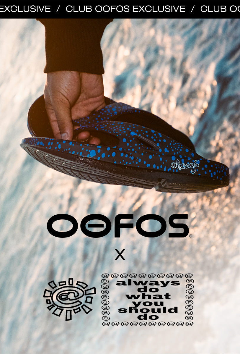 A hand holding a blue and black speckled Oofos flip-flop sandal against a beach background, with Oofos branding and slogan text overlaid on the image.
