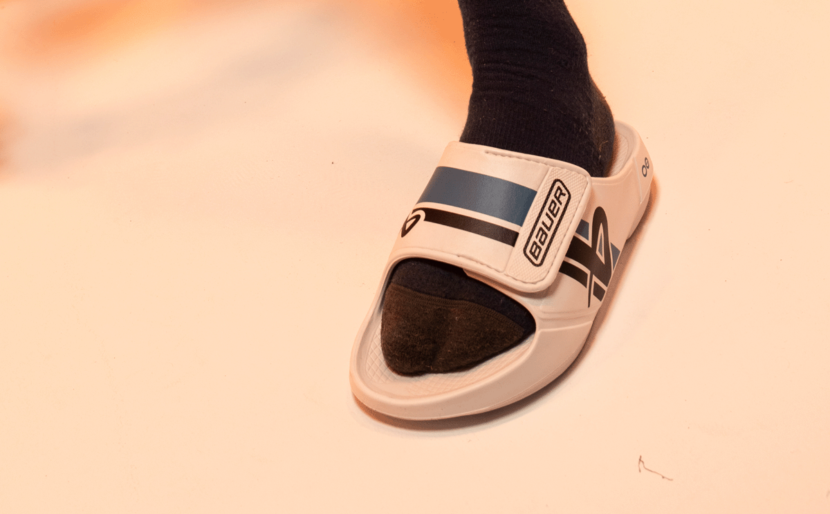 BAUER/OOFOS Men's OOahh Sport Flex Sandal – White close up of shoe on models foot in studio | lifestyle