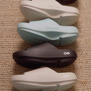 Set of four pairs of sandals in different colors on a textured surface.