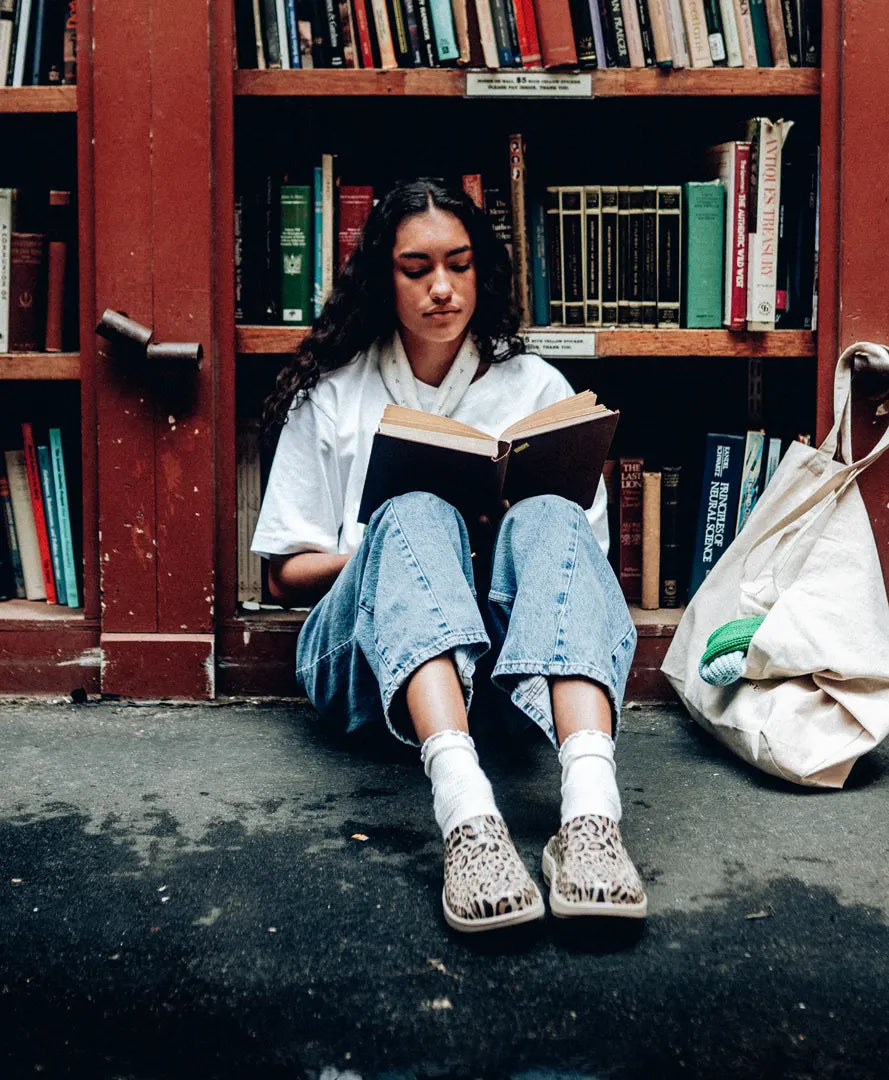 student sitting in library reading wearing nomad leopard clogs