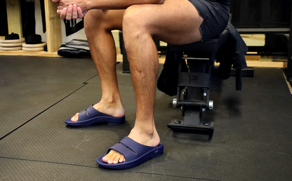 Men's OOahh Slide Sandal - Navy model wearing shoes sitting in gym | lifestyle